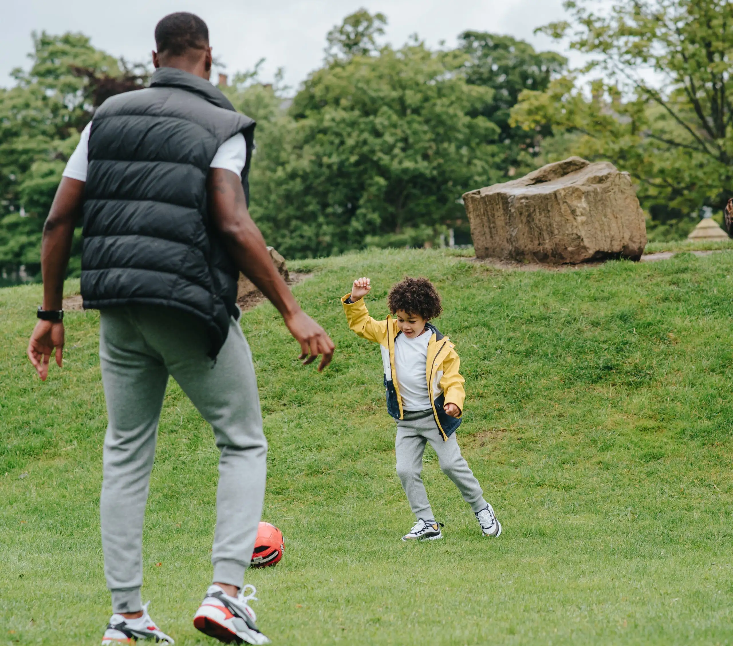 A man and child playing soccer in the park.